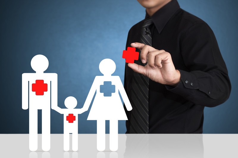 A paper doll family holding hands with a man in a black tie and shirt putting a red cross on their chests
