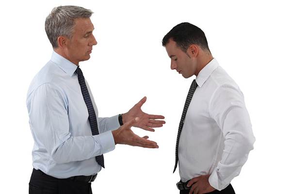 Two men in ties talking--younger one looks ashamed