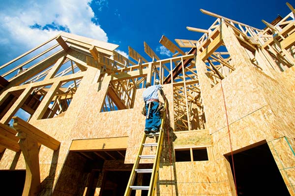 A construction worker climbing a ladder and installing plywood to the exterior of a building
