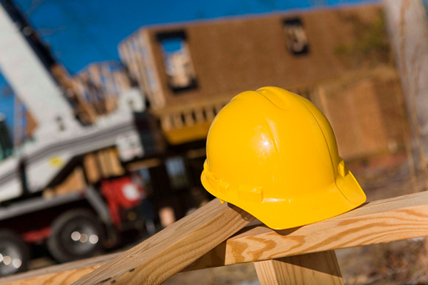 A yellow hard hat lying on top of boards with a construction site in the background