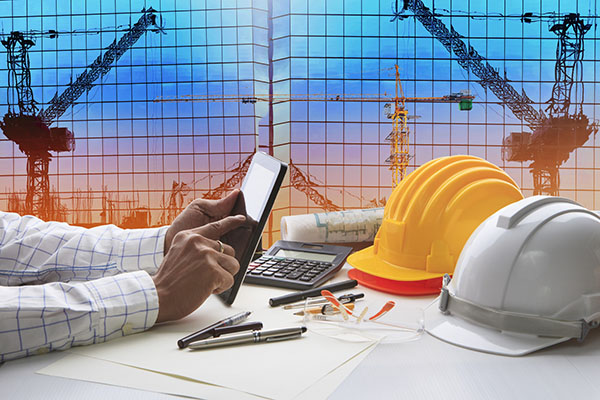 Hand of architect working on table with tablet computer and working tools against reflection of office building and crane construction