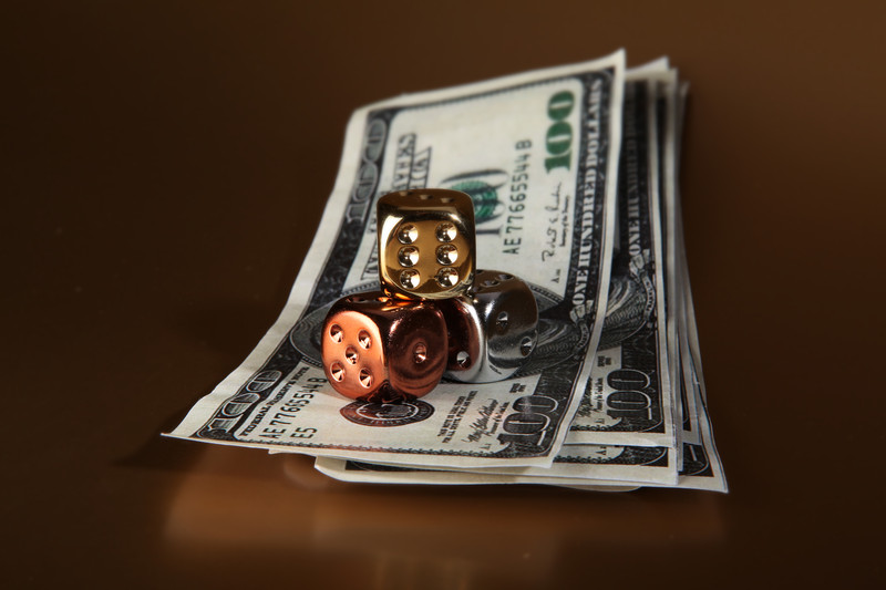 A pile of $100 dollar bills with gold, bornze, and silver dice on top of them