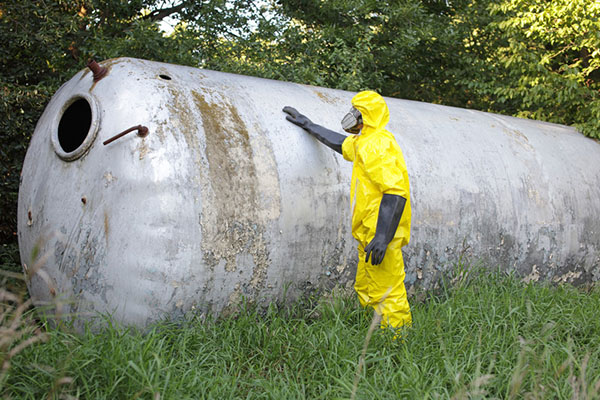 Technician in a yelllow biosuit examining a tank