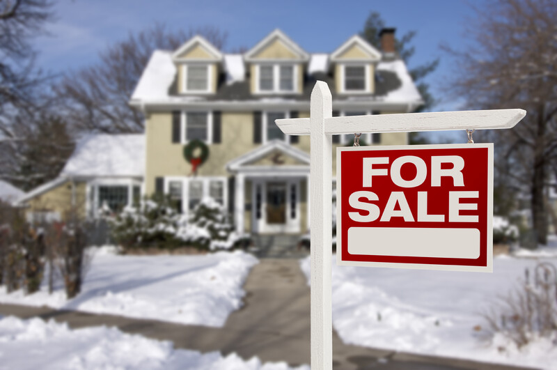 House with a for-sale sign surrounded by snow