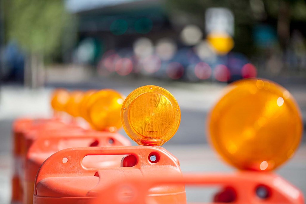 Row of Orange Construction Safety Barrier Barrels at Side of Busy Street