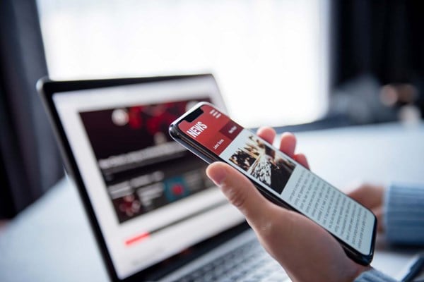 Woman reading news article on mobile screen and laptop