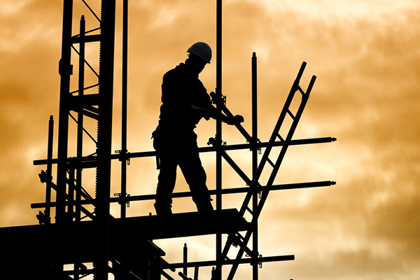 Silhouette of a construction working onscaffolding against yellow clouds