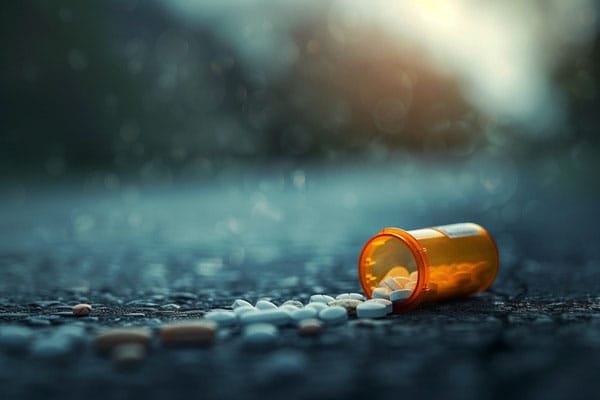 An orange prescription bottle lays open, spilling pills onto the ground