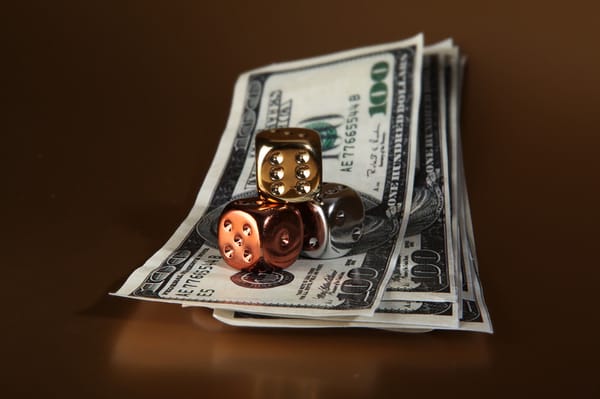 A pile of $100 dollar bills with gold, bornze, and silver dice on top of them