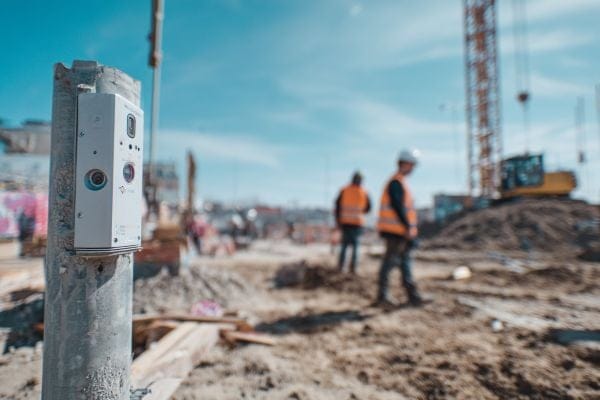 Sensor on a pole on a construction site with workers and a crane in the background
