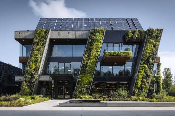 new corporate building with lots of windows, greenery on sides, and solar panels on top