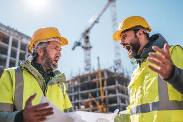 two men on a construction site yelling at each other over blueprints with a crane and partially-constructed buildings in the background