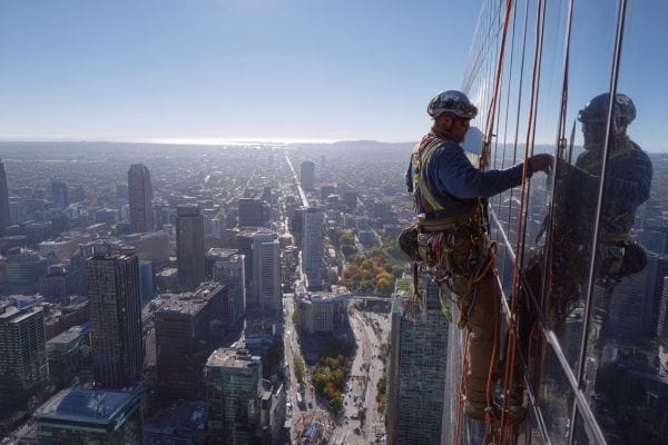 a construction worker tethered to the outside of a very high building overlooking a city