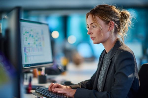 businesswoman typing on a keyboard looking at screens with data and charts