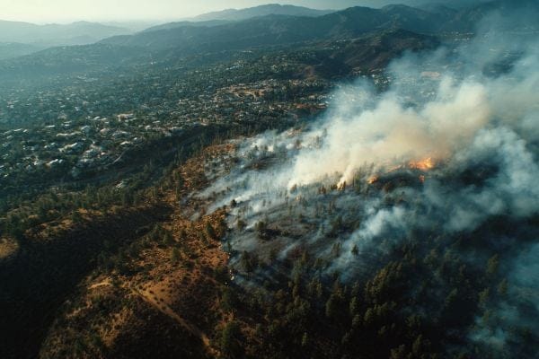 Overhead view of a wildfire burning in a forested area heading towards a town