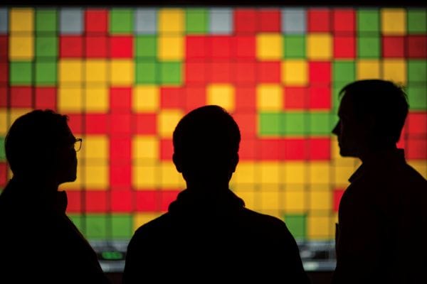 silhouettes of three business professionals looking at a wall screen filled with red, yellow, and green squares representing an insurance risk map