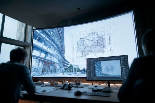 Two architects looking at two screens with renderings and blueprints of a building