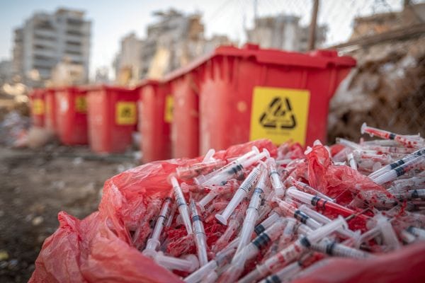 open trash bag of medical waste in front of a line of hazardouse waste garbage bins behind a hospital
