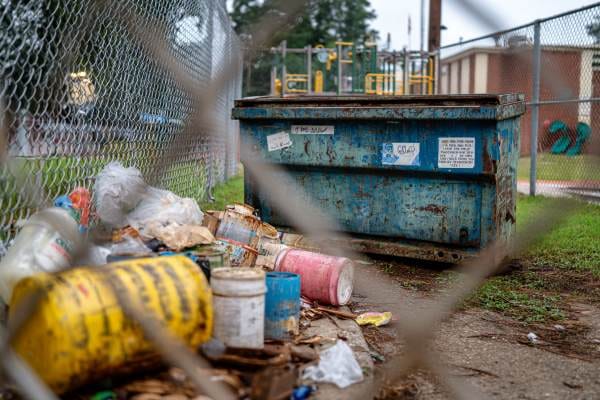 waste and chemical containers beside a trash dumpster outside an elementary school and playground