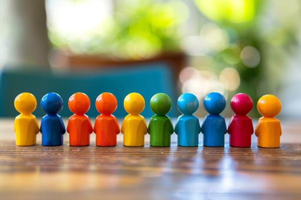 Multicolored people figurines are lined up next to each other on a wooden surface