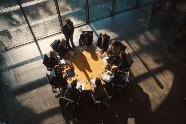 businesspeople sitting around a round table listening to a standing businessperson