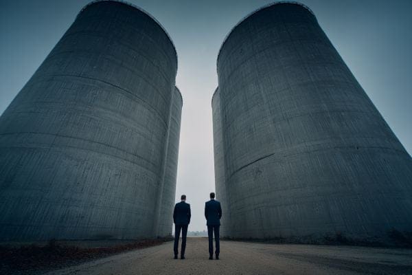 two business people standing in front of and looking up at
                    four separate silos