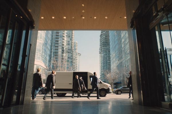 businesspeople entering a white commuter van in front of the entrance to an office building