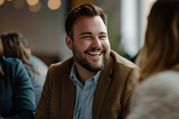 A businessman laughing while seated at a table with other people